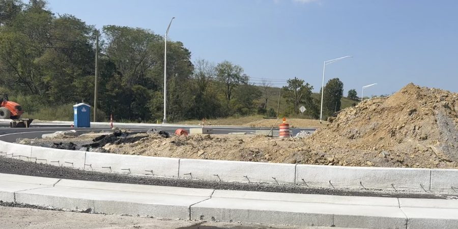 The center island of a roundabout under construction: new concrete curb with tie bars still exposed, and a heap of spoil where the island will be.