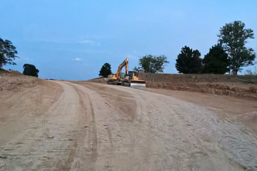 An excavator parked on a graded ridge above a dirt haul road cut through the corridor.