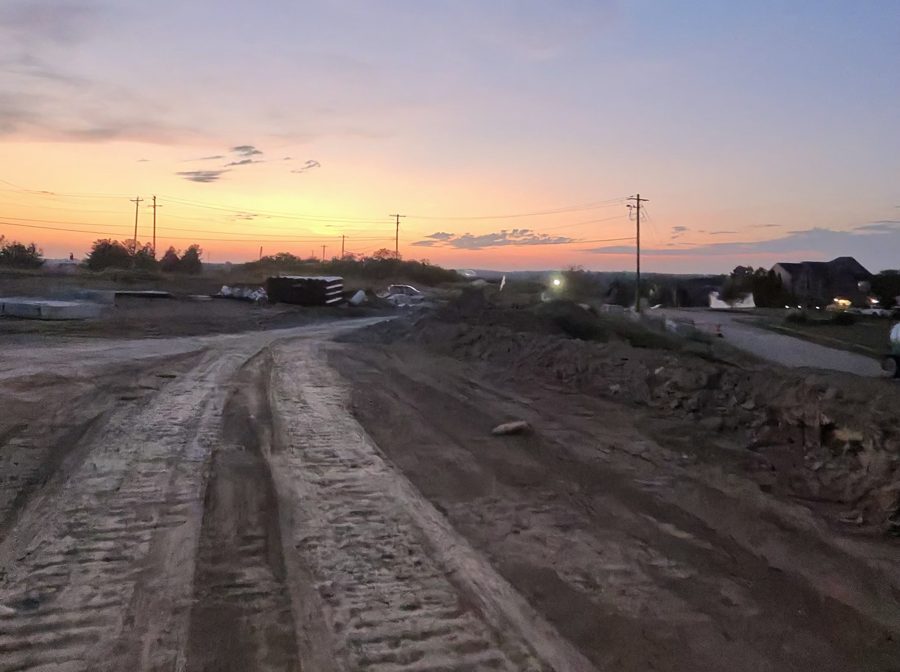 The graded haul road at sunset, running past an existing neighborhood on the right.